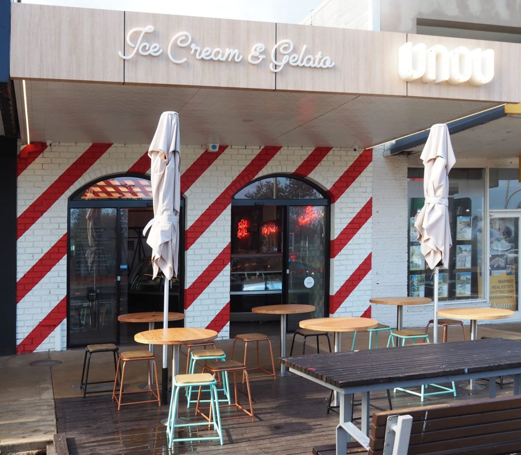 Gelato UNOU's red and white striped exterior overlooks a sunny deck. Perfect for enjoying a sweet treat.